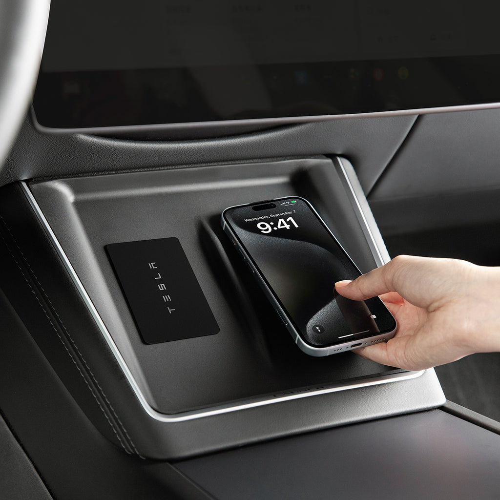 Hand placing a smartphone on a wireless charging pad in a Tesla vehicle.
